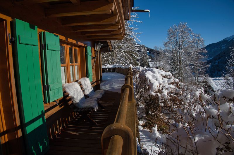Besneeuwd balkon met groene luiken en uitzicht op de bergen